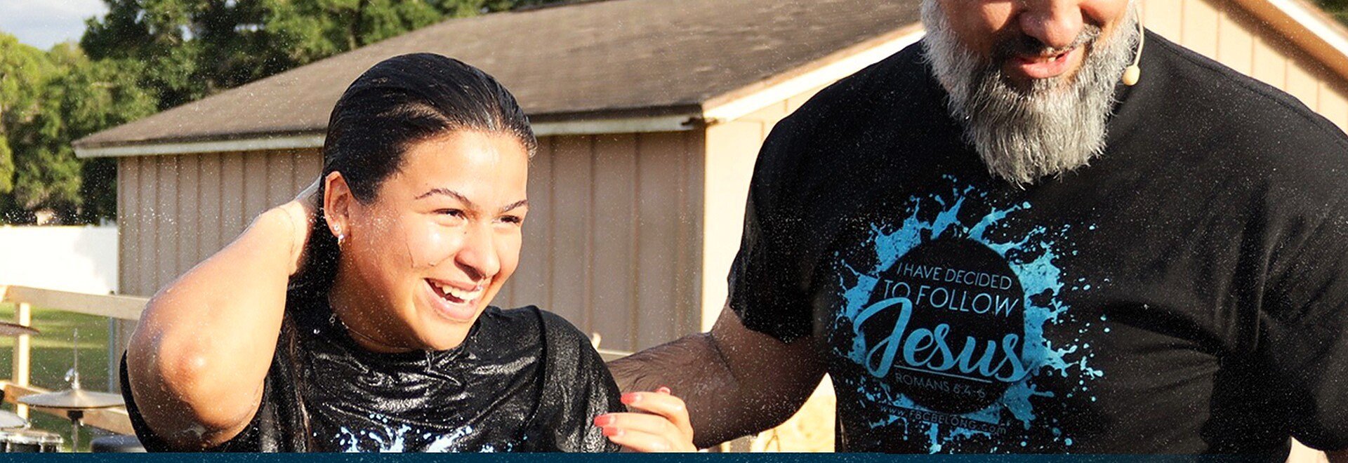 A smiling woman being baptized beside a bearded man in a Jesus t-shirt