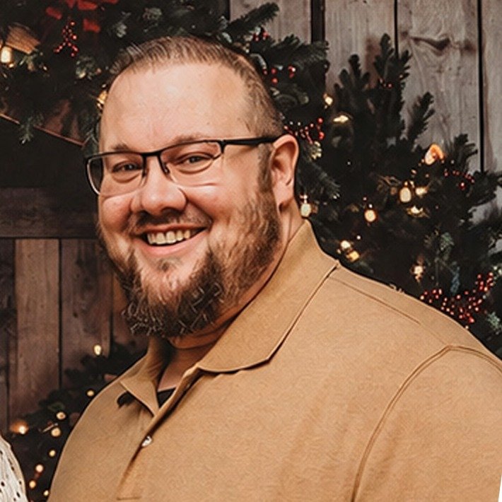 Portrait of a smiling bearded man with glasses in a tan polo shirt
