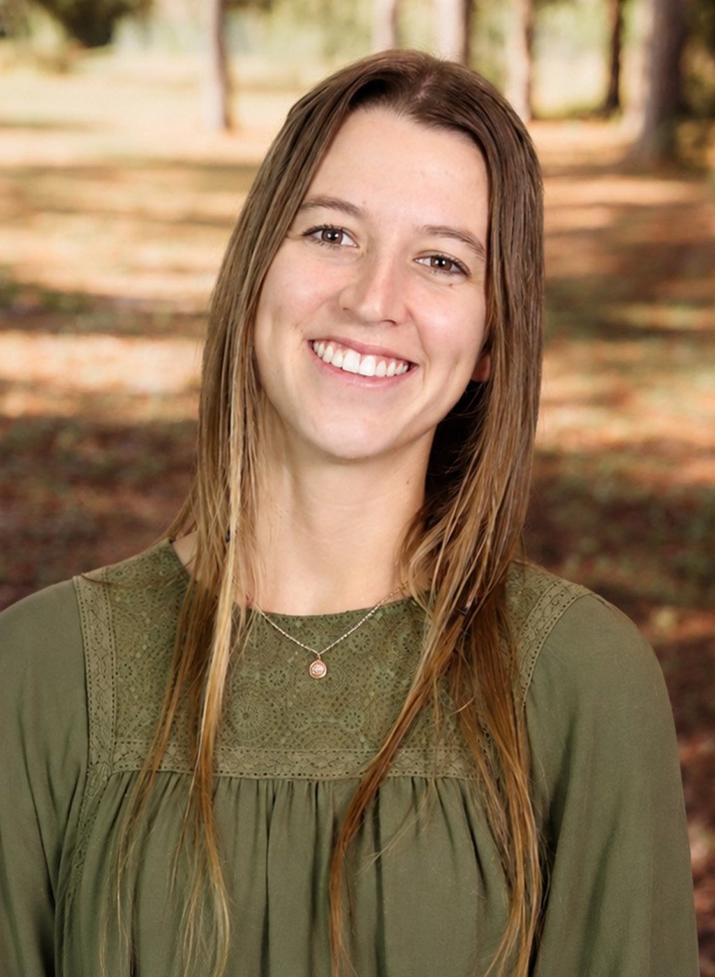 Portrait of a smiling woman with long light brown hair in an olive top outdoors