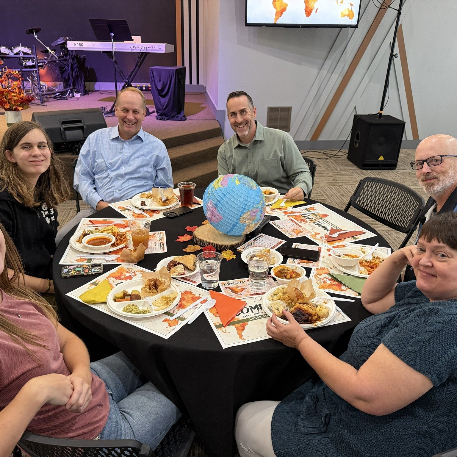 People seated around a decorated table sharing a meal in a church room