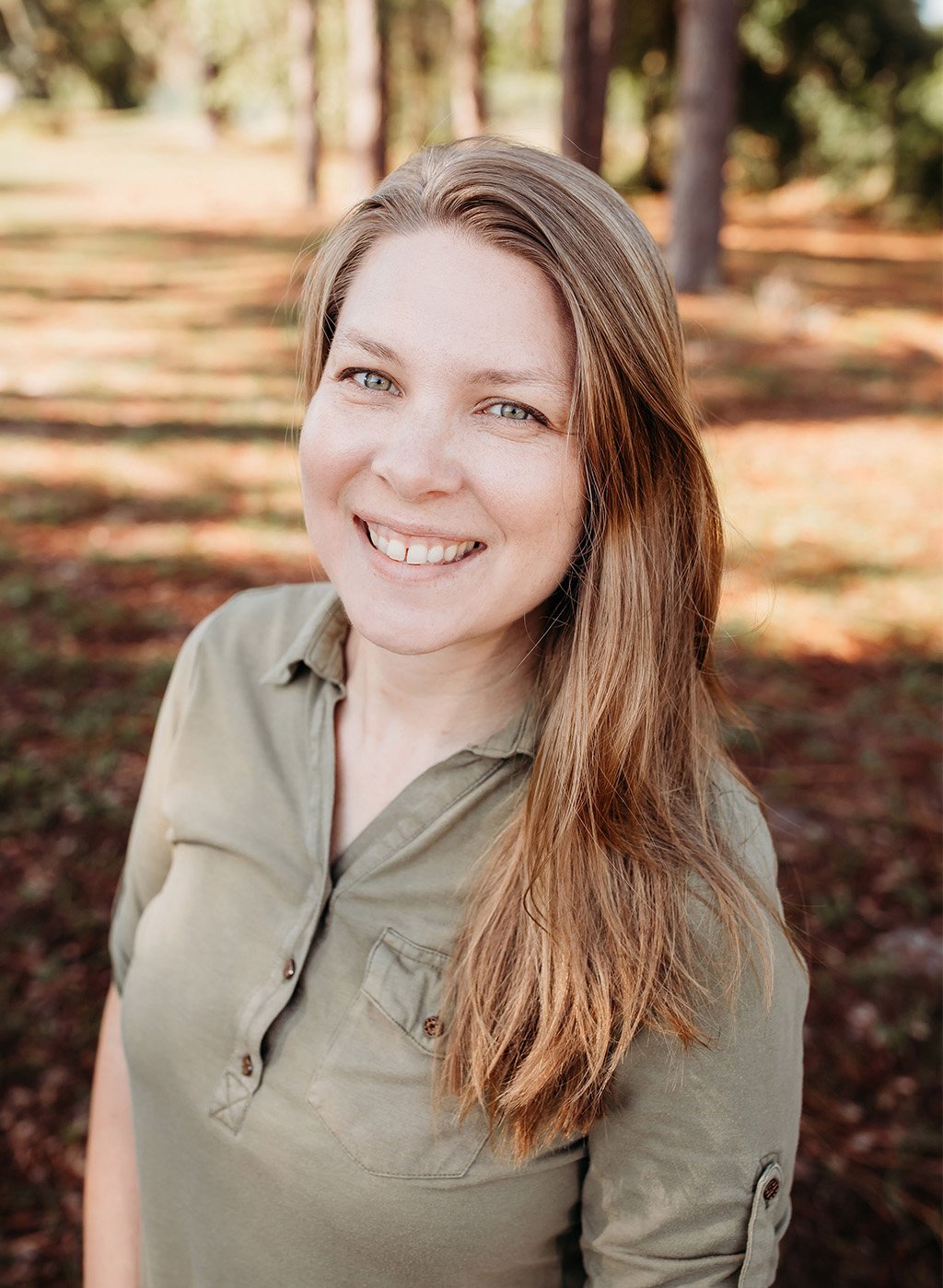 Portrait of a smiling woman with long light brown hair in an olive button shirt outdoors