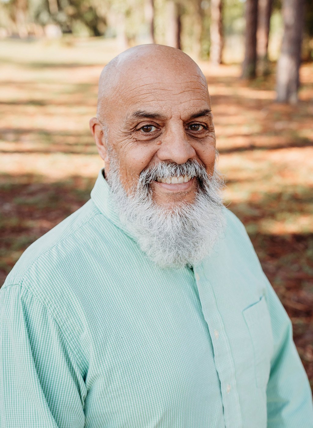 Portrait of a smiling bald man with a gray beard in a light green shirt outdoors