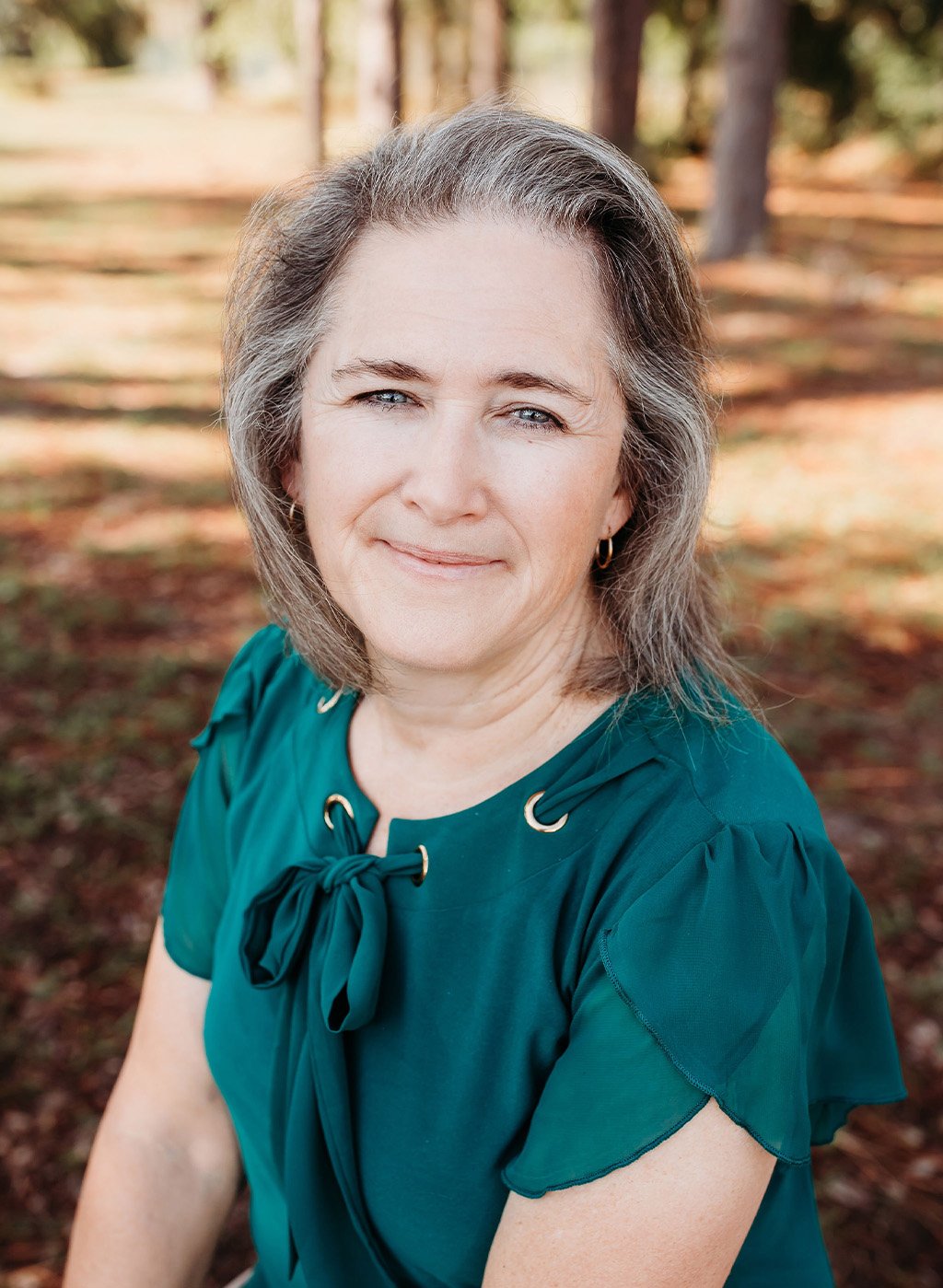 Portrait of a smiling woman with gray hair in a teal top outdoors