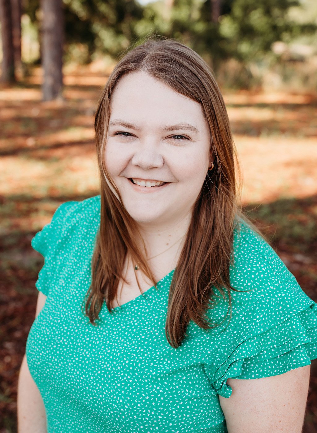 Portrait of a smiling woman with long brown hair in a teal top outdoors