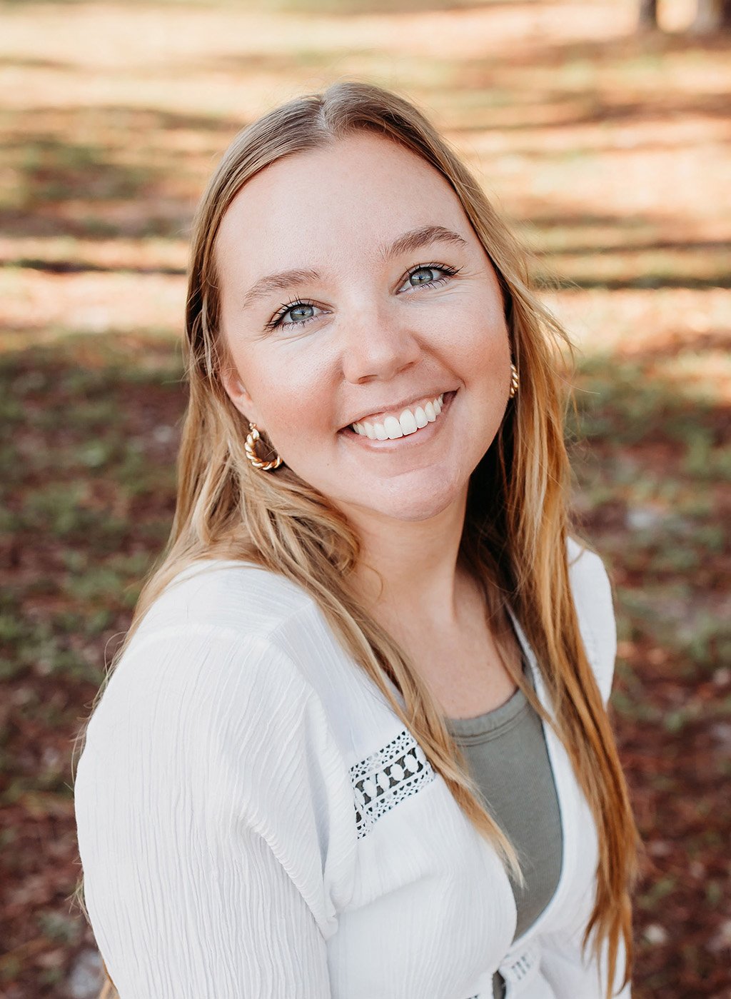 Portrait of a smiling woman with long blonde hair in a white jacket outdoors
